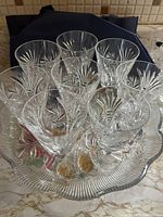 Photo showing eight clear crystal wine glasses with 8 pinwheel cut pattern arranged on colorful round crystal tray with floral center pattern.