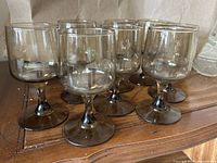 Eight brownish-colored wine glasses grouped on a wooden surface, showing front and side views of the glasses.