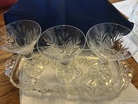 Three clear crystal martini glasses with pinwheel and starburst cut pattern on a matching clear crystal tray with floral pattern and handles.