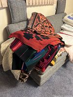 Stack of various woven and knitted blankets and throws with geometric and striped patterns on a sofa