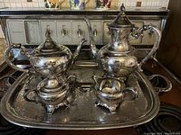 Front view of the silver coffee pot, teapot, creamer, sugar bowl arranged on the large silver tray showing ornate decorative handles and detailed design