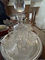 View of the set of six whiskey glasses, crystal decanter, and silver-plated round tray from an angle showing the detailed etched glass and tray rim.