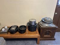 Photo showing multiple roasting pots and baking pans arranged on tables, including stack of metal trays and pots.