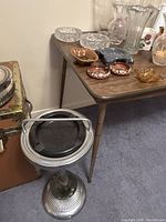 Multiple ashtrays of varied materials and designs on a wooden table, including glass, ceramic, wood, and crystal