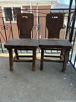 Photo of two dark wood chairs with cutout handles in the backrests, showing wear on surfaces and legs.