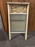 Frontal view of vintage washboard showing wooden frame, glass ridged washing surface and printed label on wooden top panel.