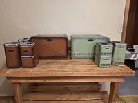 Two sets of vintage kitchen canisters including bread boxes and smaller canisters in green and brown colors on wooden bench.