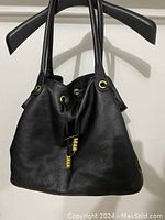 Front view of large black leather purse with two shoulder straps and visible gold eyelet and bead details on the drawstring closure.
