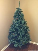 Full assembled artificial Christmas tree with pine cones visible on branches, positioned in corner against beige walls.