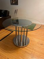 Photo of the glass top dining table showing clear glass top and silver base in room with wooden floor