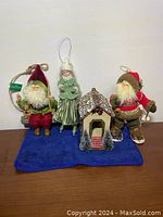 Lot of 4 vintage Christmas hanging ornaments displayed on blue cloth: two Santa Claus figurines, one skater girl figurine, and one chalet house ornament.