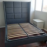 Full view of the queen size bed frame showing tall grey fabric headboard and wooden slats