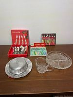 Overview of entire lot with boxed cutlery sets, glass serving pieces, and metal butter dish