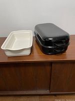 Photo of cream ceramic casserole dish and two stacked black enamel roasting pans with lids on wooden surface