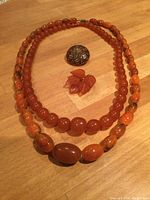 Top view of two amber bead necklaces surrounding two pins on wooden surface