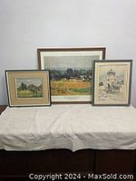 Three framed prints displayed side by side on a soft white cloth, showing a farm scene, winter sleigh scene, and Hermitage Museum art.
