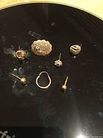 Seven single gold earrings displayed on a black surface.