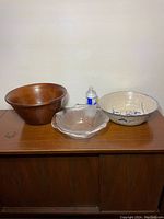 Photo of three serving bowls: wooden, glass with seashell ridges, and floral pottery bowl, arranged side by side with a water bottle for scale.