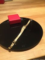 Vintage ladies Bulova wristwatch laid flat on a black reflective surface along with a red patterned box.