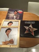 Four vinyl album covers on wooden table showing Julio Iglesias, Dean Martin, and Starburst albums