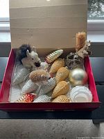 Box containing woodland animal ornaments, pine cone shaped ornaments in gold and silver, and spherical baubles.