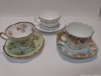 Three bone china teacups and matching saucers shown together, highlighting design differences and condition
