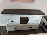 Front view of wooden dresser showing distressed white finish and central black metal mesh door with multiple drawers and black handles.