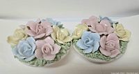 Pair of floral ceramic candle holders with multiple pastel flowers on leafy bases, viewed from front