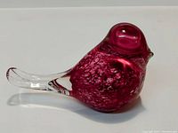 Side view of red glass bird figurine showcasing mottled red coloration and clear tail portion, on neutral background.