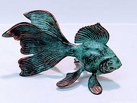 Metal fish sculpture with blue-green patina and copper accents, showing side and top view details of fins and body.