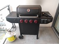 Front view of a black propane barbecue grill with four red knobs and a temperature gauge on the lid, showing overall condition and features.