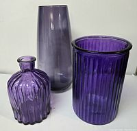 Photo showing three purple glass vases of different shapes and sizes against white background.