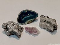 Four mineral specimens displayed on neutral background: blue-green sliced geode, metallic silver mineral, amethyst quartz cluster, white quartz rock.