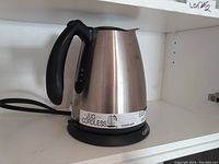 Stainless steel cordless jug kettle on base with black plastic handle, spout, and cord.