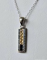 Close-up of rectangular sterling silver pendant with sapphire, citrine, and white stones.
