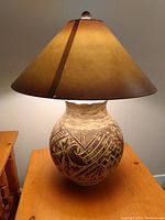 Table lamp with ceramic base decorated with black tribal-style patterns and a large brown conical fabric lampshade; lamp is lit.
