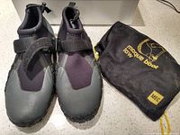 Pair of black and gray water shoes with adjustable straps alongside carrying bag
