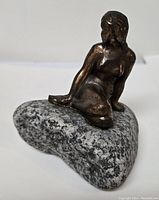 Figurine of a copper woman seated on heart-shaped stone base showing front-side view