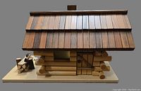 Side view of the wooden log cabin showing the detailed wooden door, logs, and woodpile accessory on the base