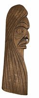 Photo of a brown wooden carving approximately 22 inches in length, shaped as a highly stylized human face in profile with detailed grooves and a pronounced nose and eye.