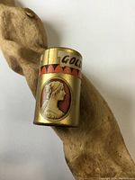 Front view of antique golden cylindrical matches case showing cameo portrait and partial text 'GOLDEN'