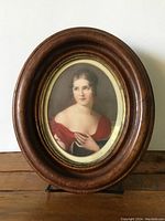 Front view of the antique oval wood frame with portrait picture, showing woman in red dress.
