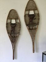Pair of antique wooden snowshoes hanging on a wall, showing full size and shape.