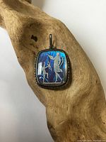 Pendant shown on wooden surface highlighting butterfly wing inlay with cupid design and silver frame