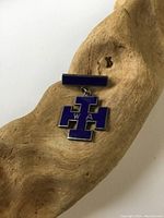 Front image of the Birks sterling silver blue enamel cross badge resting on a piece of wood, showing details of the blue enamel and cross shape with letters.