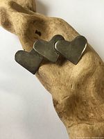 Front view of Birks sterling silver triple heart brooch displayed on a wood background showing connected hearts and tarnished surface.