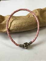 Pink braided rope bracelet on a natural wood background showing hexagonal sterling silver clasp with 'PANDORA' engraving.