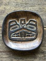 Front view of small square clay dish with raised Haida Beaver design, dark brown and black glaze.