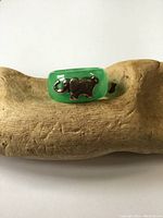 Green hardstone ring with a silver elephant decoration on one side, placed on a rustic wood surface.