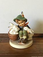 Front view of the Hummel figurine showing seated child holding and sitting near two white rabbits, one in a basket.